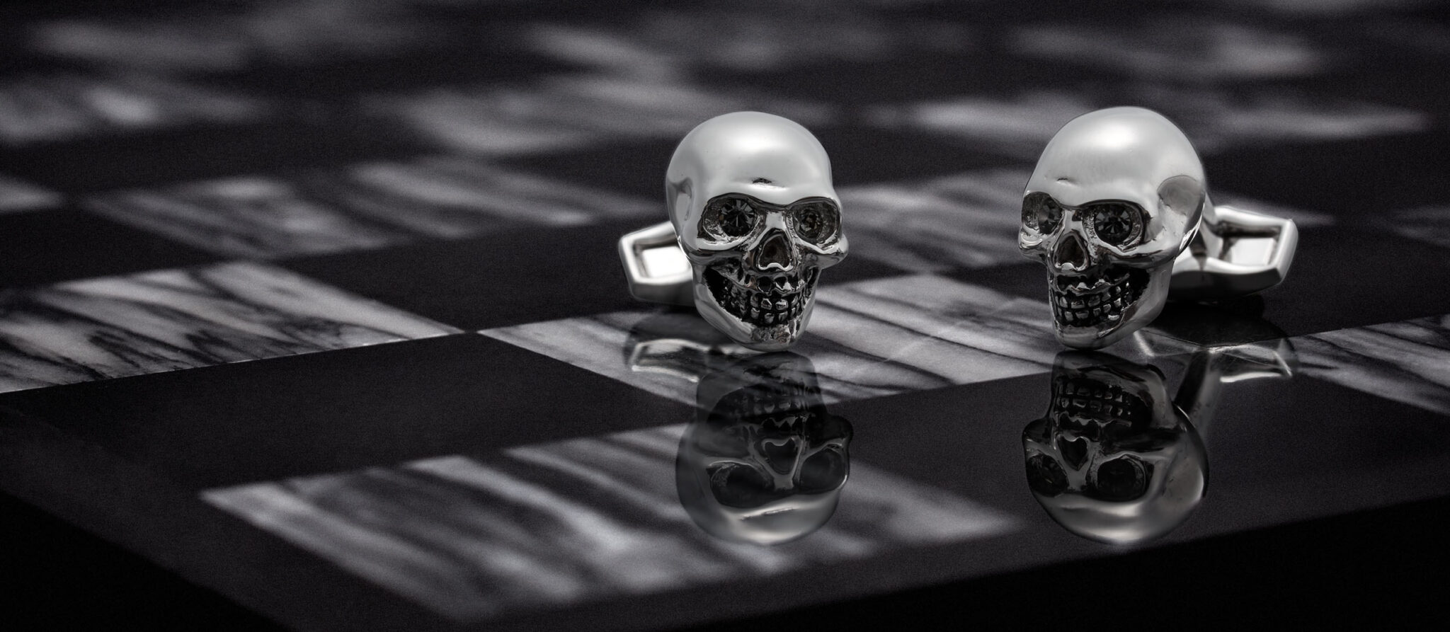 dark and moody marketing photograph of Alexander Mcqueen skull cufflinks on a black and white marble chess board