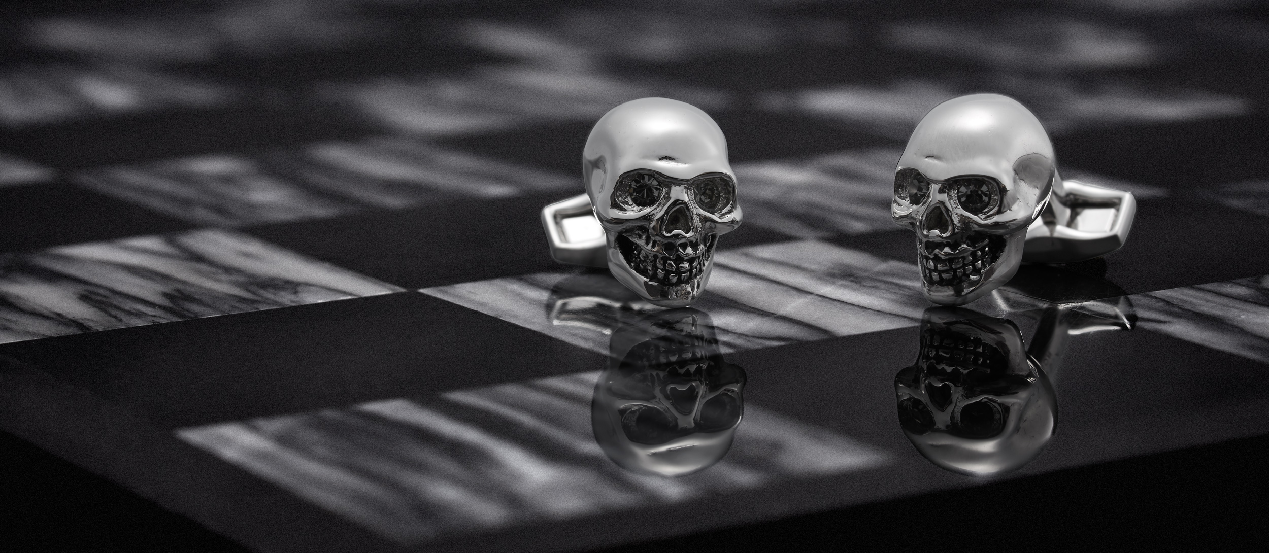 dark and moody marketing photograph of Alexander Mcqueen skull cufflinks on a black and white marble chess board