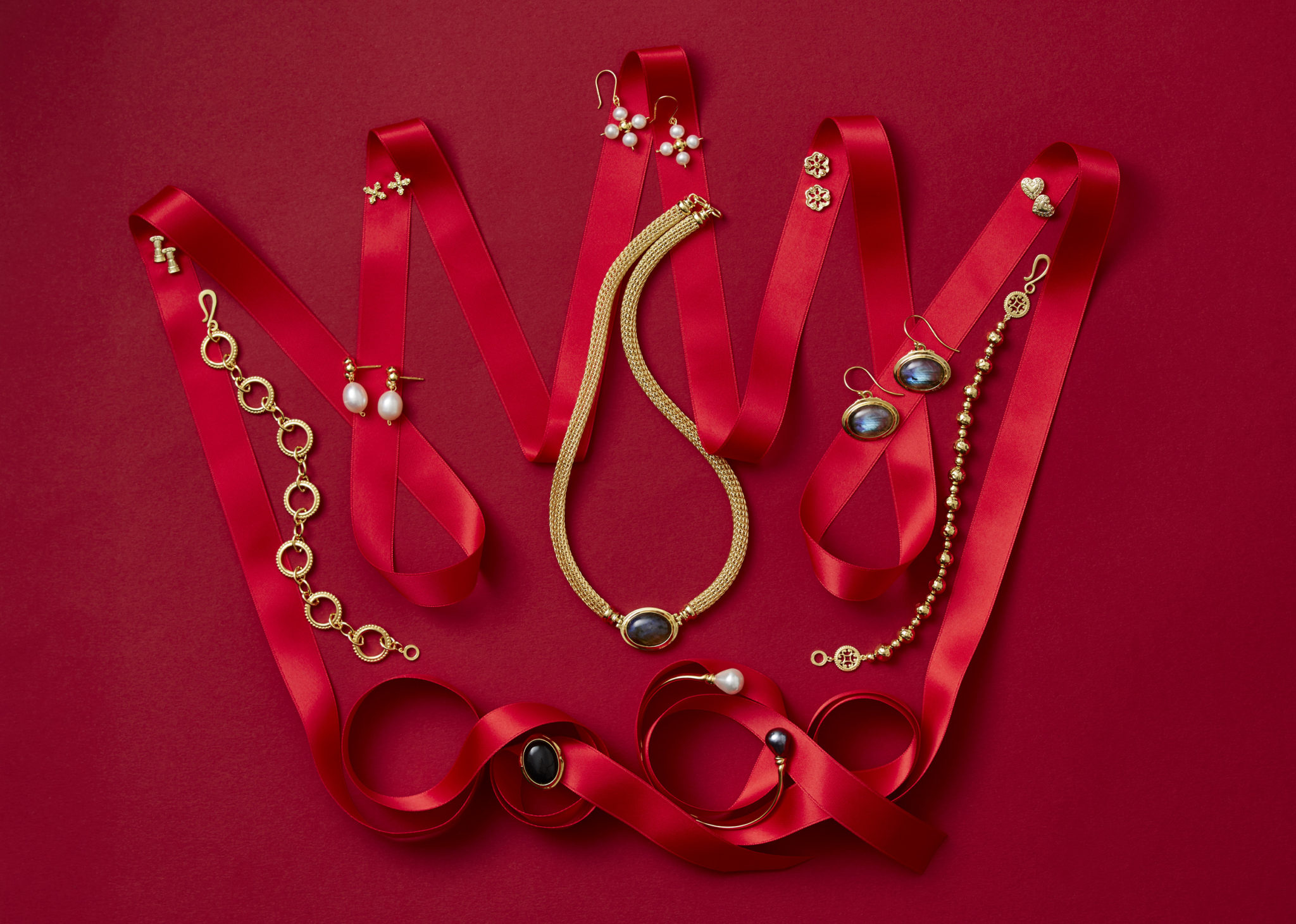 marketing still life photograph of a crown made of red ribbon adorned with gold, lapis, and pearl jewelry including earrings, necklaces, and bracelets on a red background.