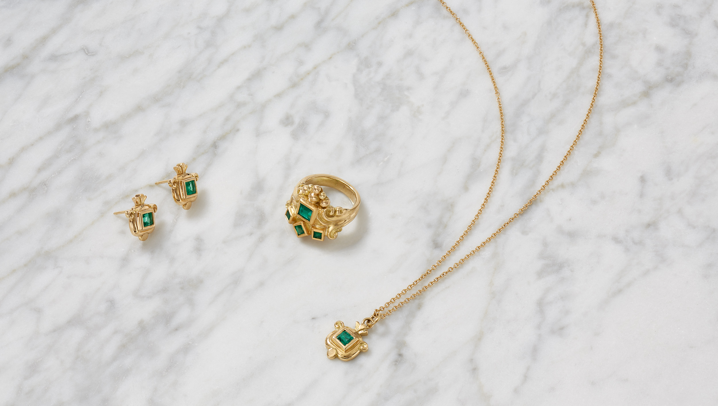 marketing still life photograph of gold and emerald jewelry on a marble background