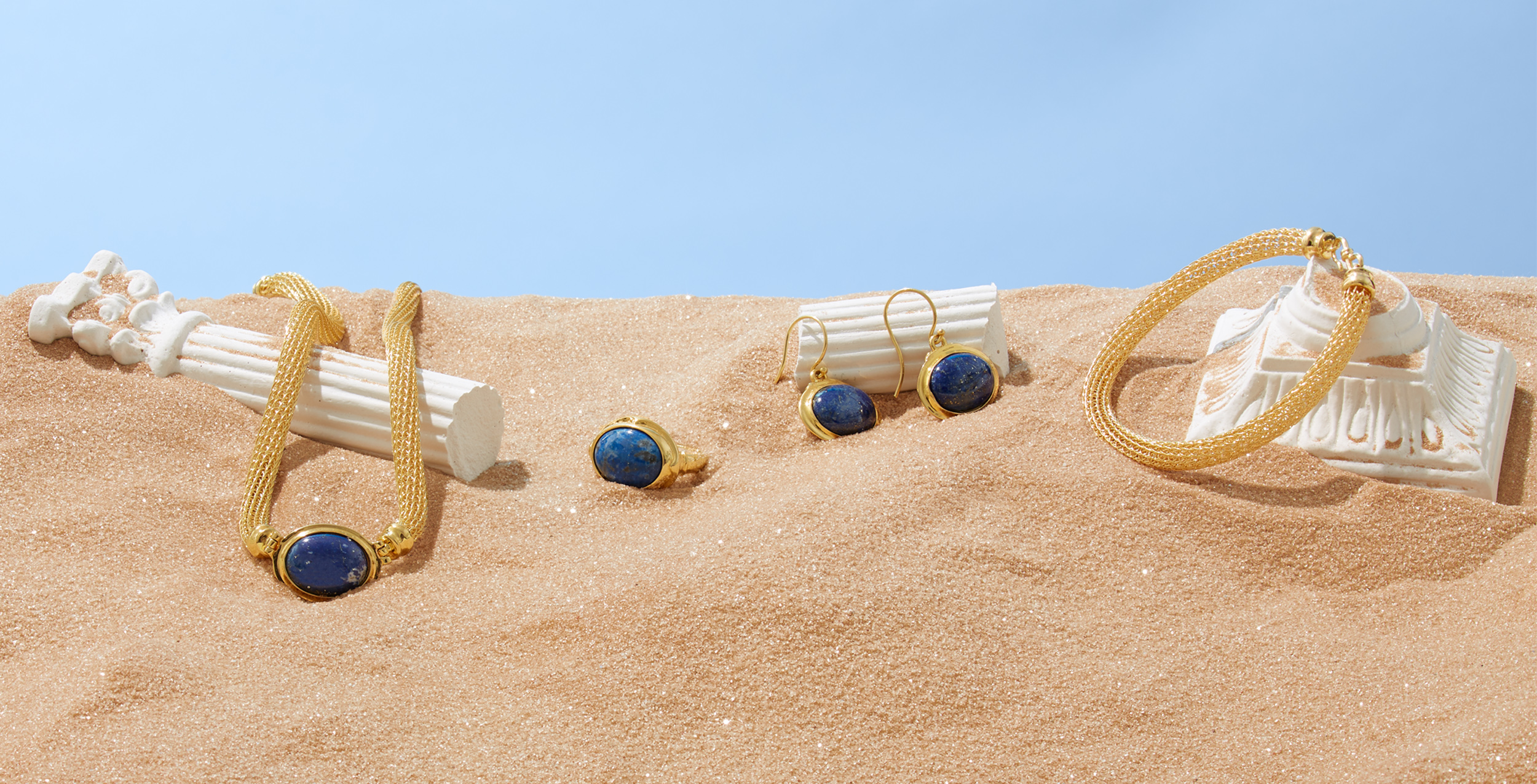 marketing still life photograph of gold and lapis cabochon jewelry draped on ruins of marble columns in the desert