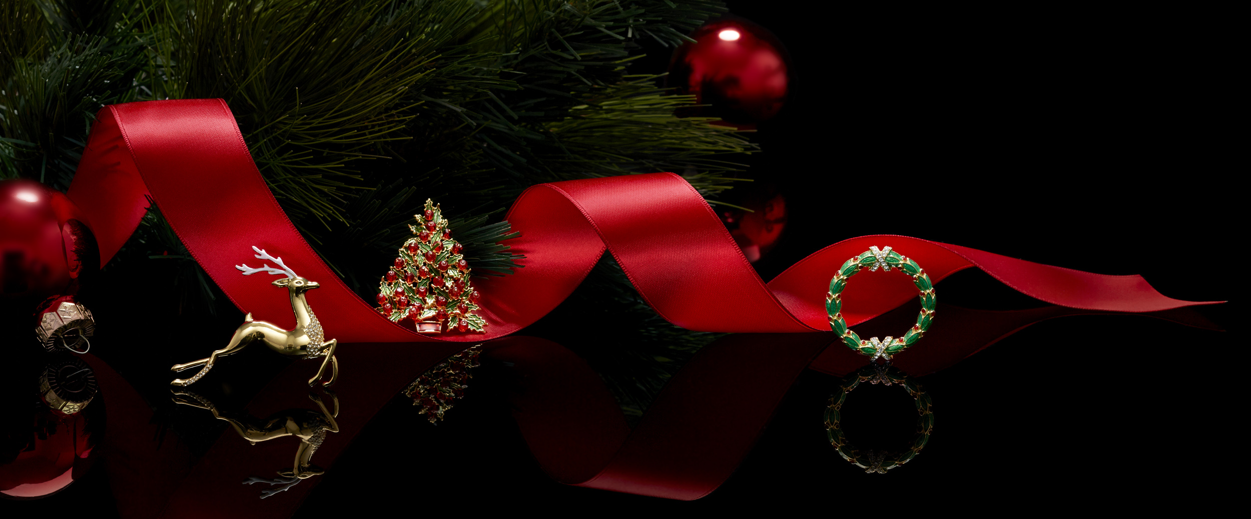Holiday pins e-commerce header with a red ribbon, tree branch, reflection, and black background