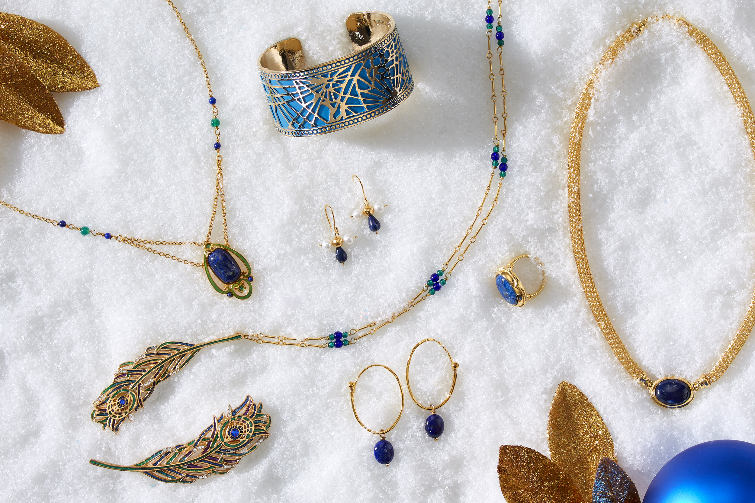 marketing still life photograph of blue, gold, and lapis jewelry including necklaces, earrings, a ring, a bracelet, and a pin on snow
