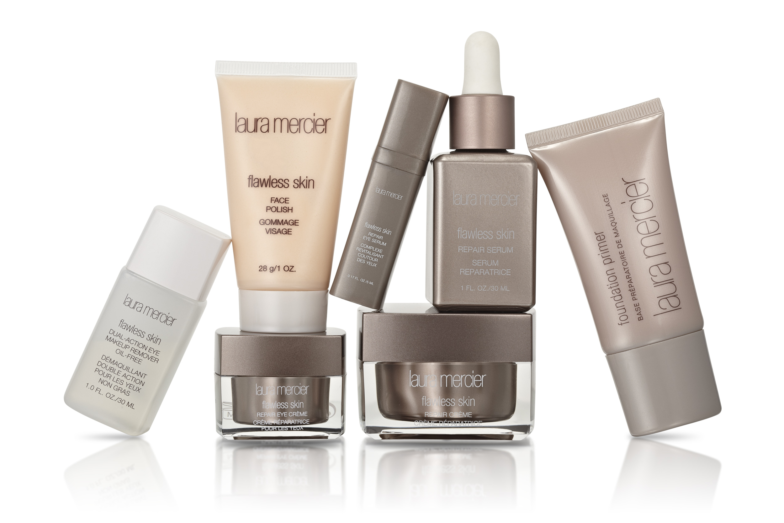 e-commerce product photograph of seven skin care products including serums, cremes, and foundation in a dynamic group composition on white with a reflection