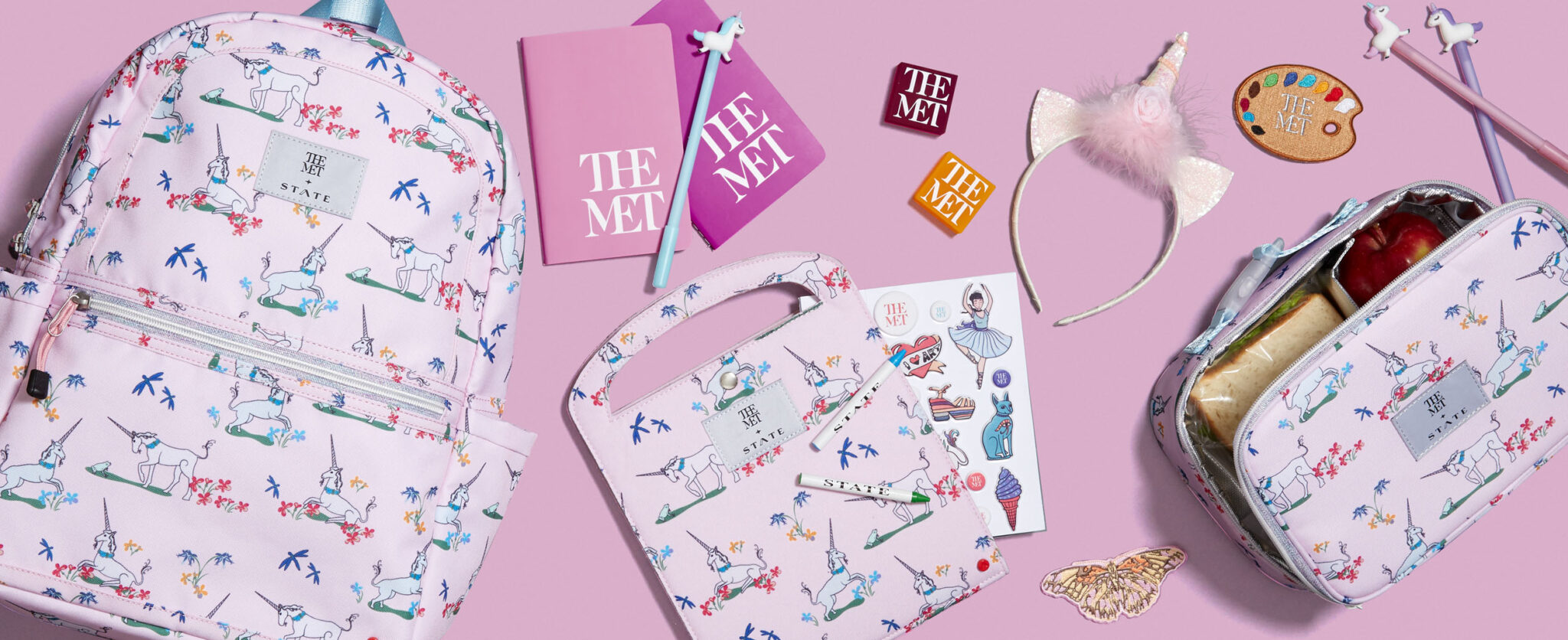 e-commerce header of the Met x State collaboration with unicorn backpack, lunch box, art folio, and supplies on pink background