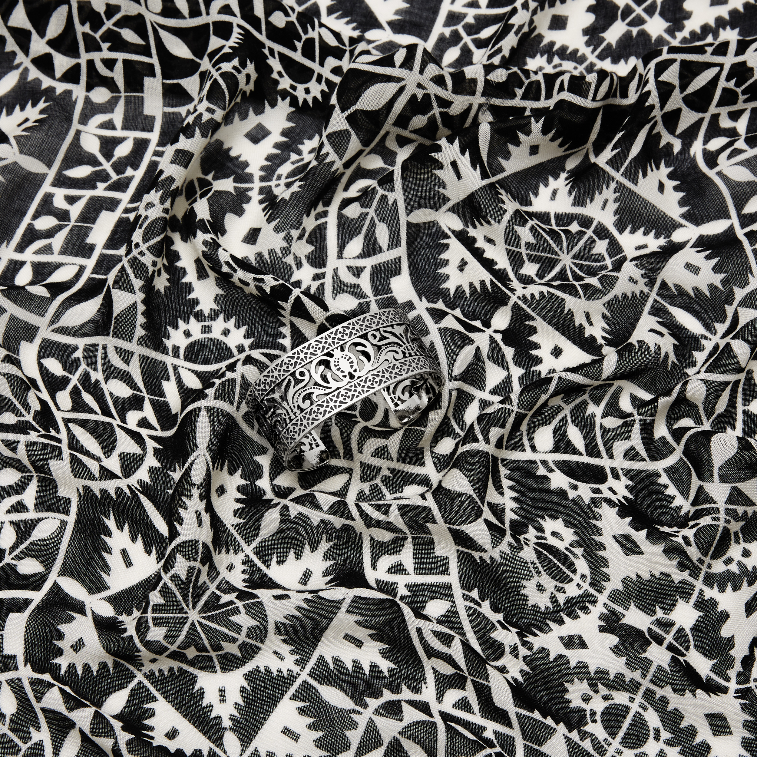 intricately patterned silver bangle bracelet on intricately patterned black and white scarf