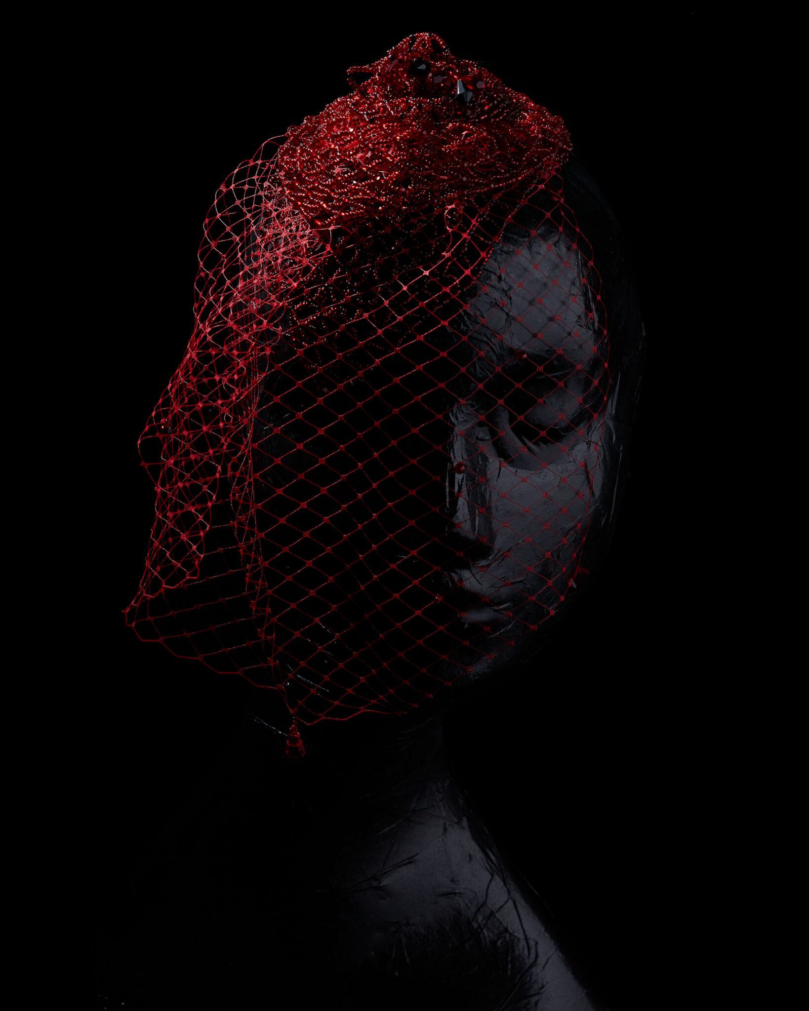 red beaded net hair piece and veil on a somber black mannequin on a black background