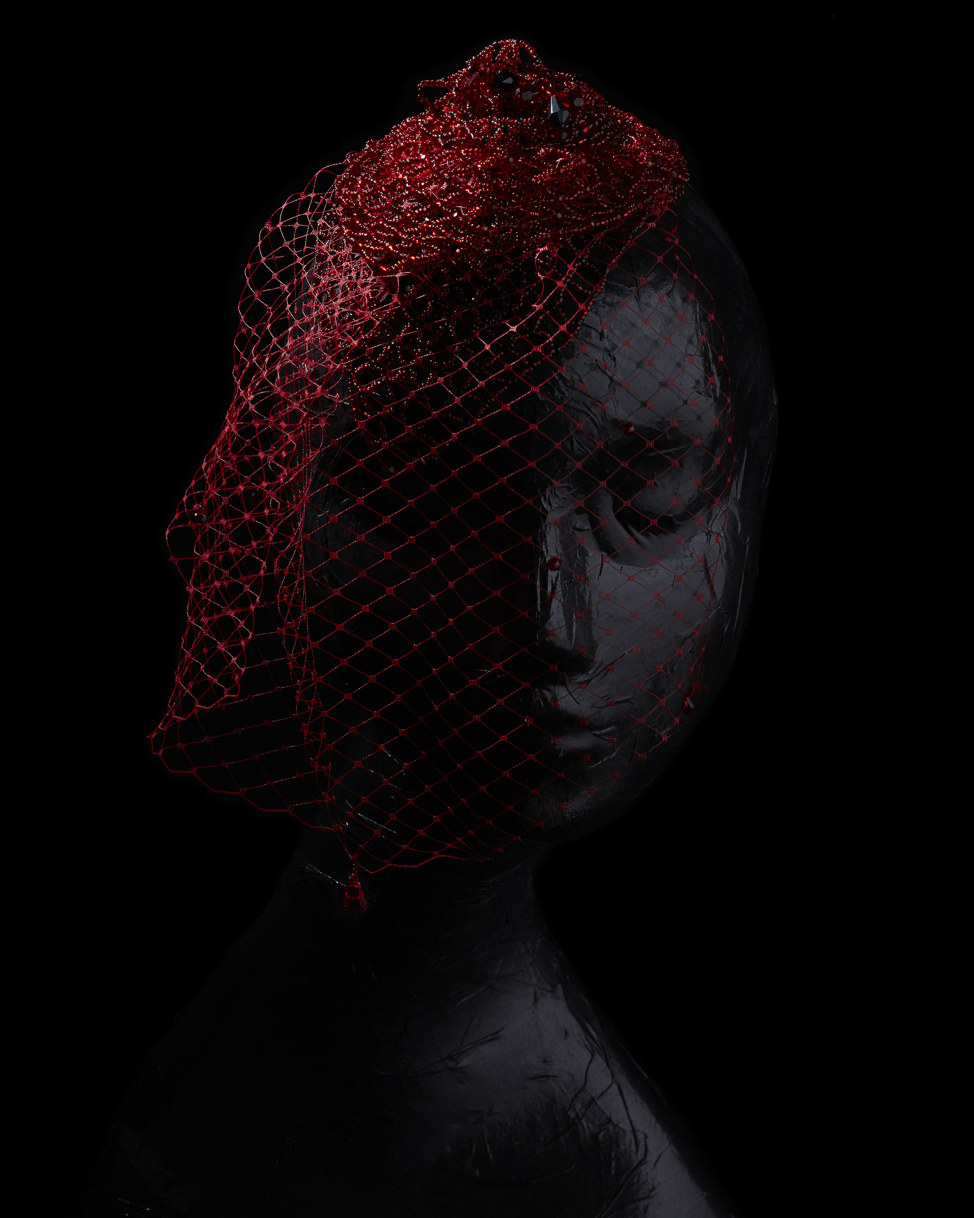 red beaded net hair piece and veil on a somber black mannequin on a black background