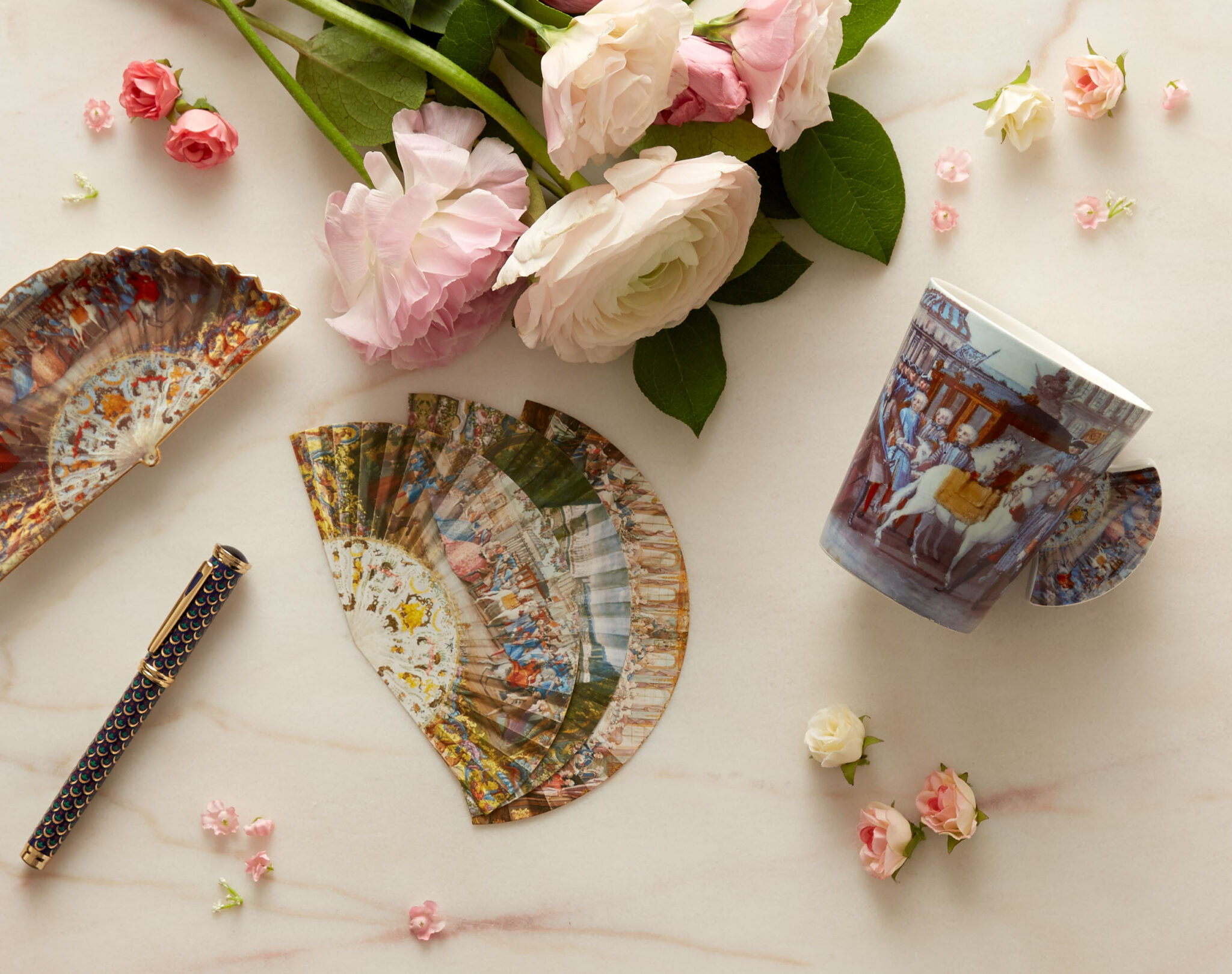 still life in warm window light of a pen, notecards, a tray, a teacup, and flowers on marble
